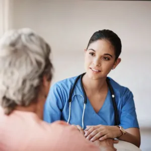 Latino Nurse in a blue scrub shirt comforting an elderly woman with her back turned.