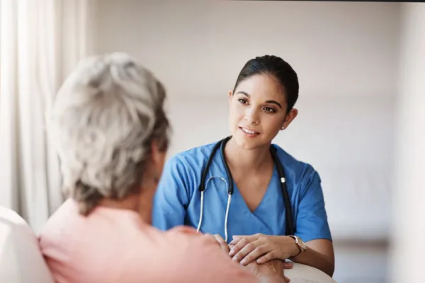 Latino Nurse in a blue scrub shirt comforting an elderly woman with her back turned.