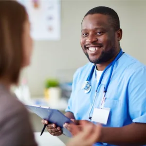 Black Male nurse in blue scrubs holding a clip board. Talking to a patient.