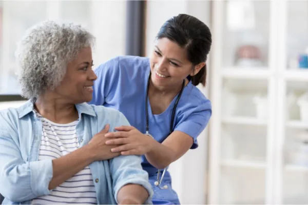 Nurse comforting a patient in a medical setting. Patient is in a wheelchair.